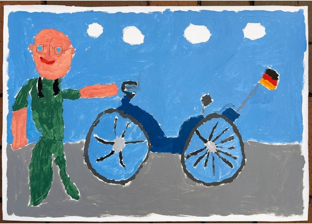 An elderly man wearing green clothing and glasses points with his left hand toward a bicycle or motorcycle and smiles. A German flag is attached to it. The sky in the background is blue, and four clouds are indicated.